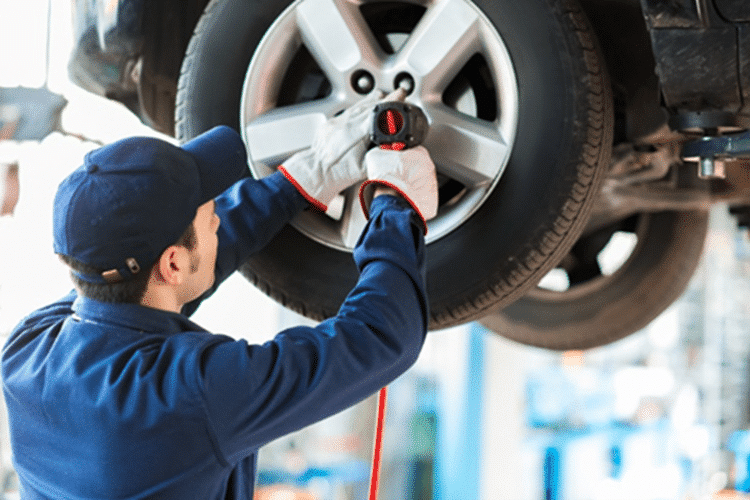 A mechanic using a drill to work on the wheels of a raised car