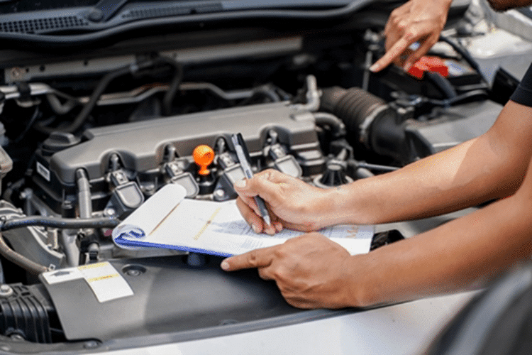 A person writing on a clipboard placed on the engine of a car.