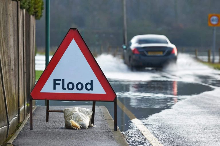Motorist driving through flood waters with warning sign in foreground